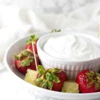 A ramekin of Coconut Whipped Cream surrounded by slices of strawberries and pineapple from acleanplate.com