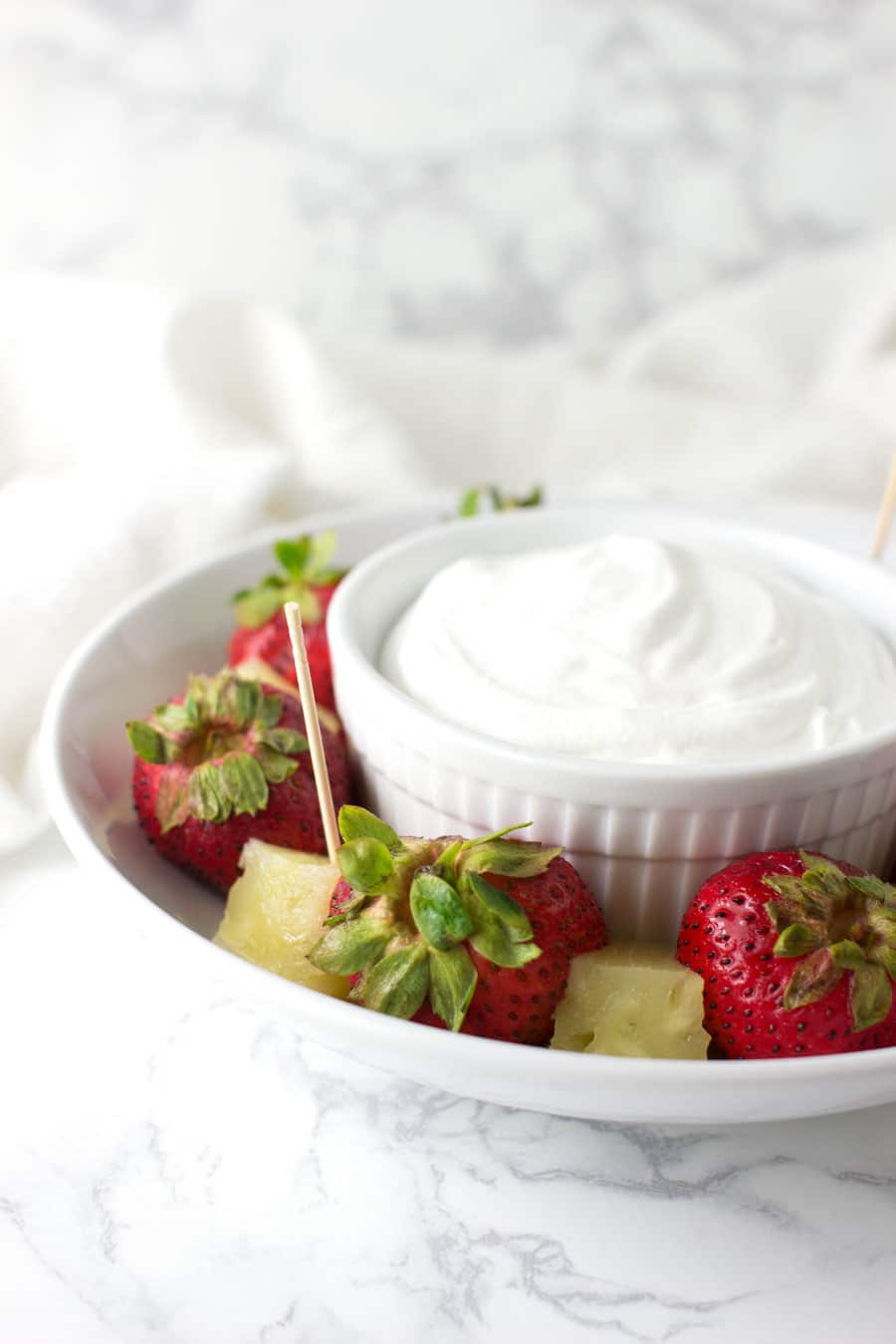A ramekin of Coconut Whipped Cream surrounded by slices of strawberries and pineapple from acleanplate.com