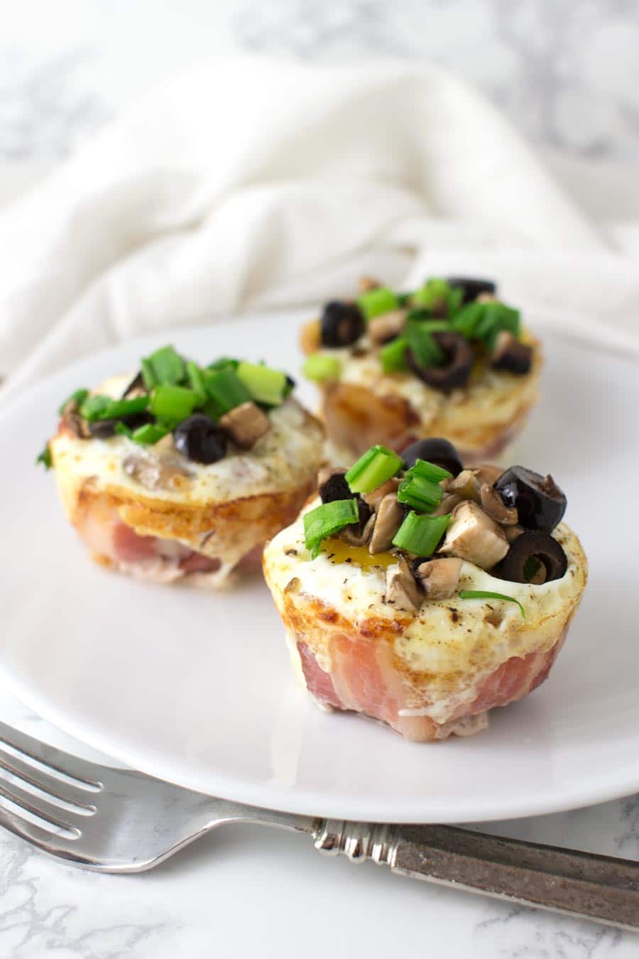 Three Bacon and Egg Muffins topped with green onion, olives, and mushrooms from acleanplate.com