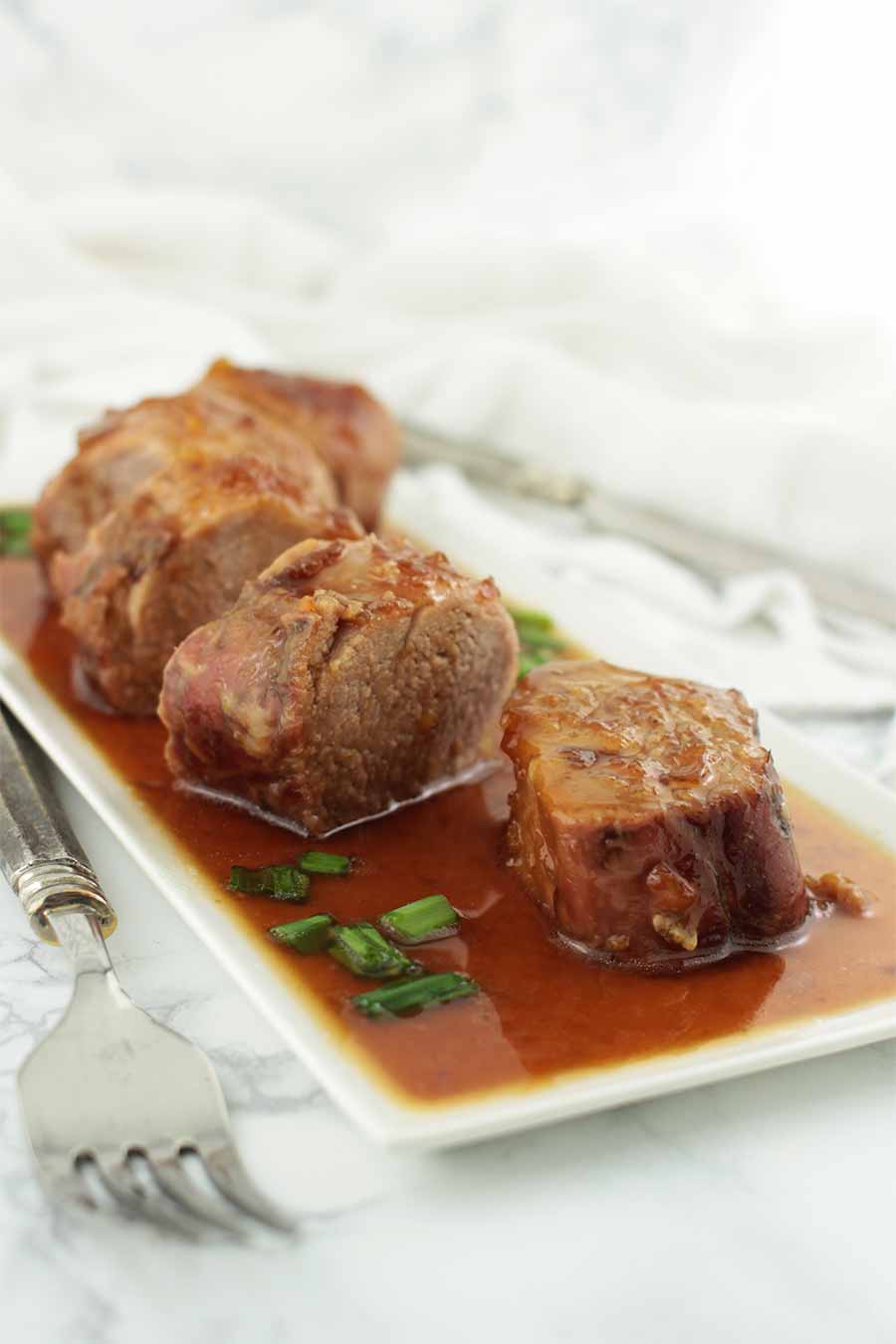 Slices of Orange-Glazed Pork Tenderloin swimming in sauce and green onions from acleanplate.com