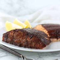 Maple-Glazed Salmon filets on a plate with lemon slices for garnish from acleanplate.com