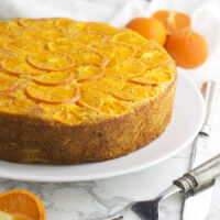 A Clementine Upside Down Cake with fresh oranges in the background from acleanplate.com