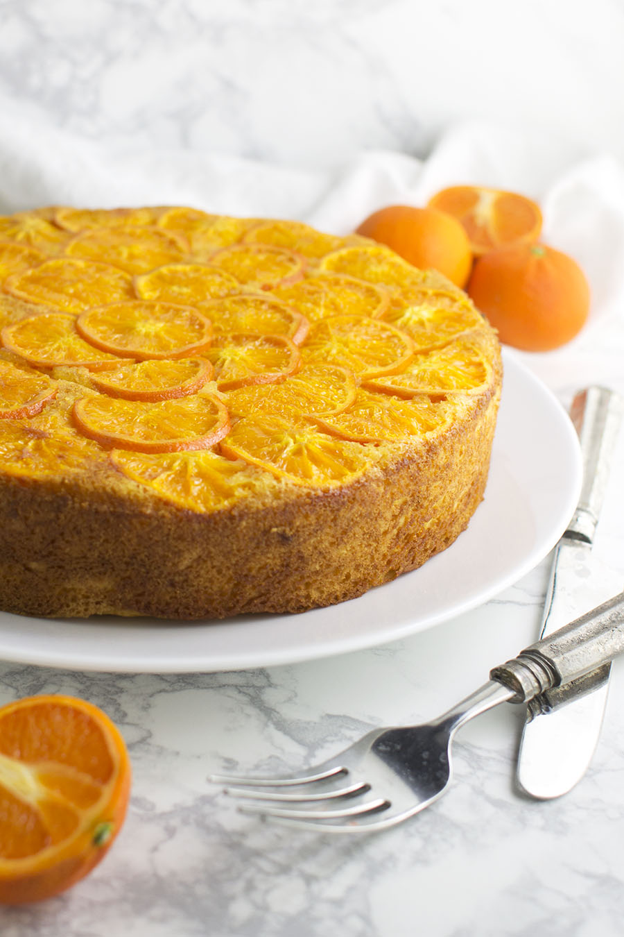 A Clementine Upside Down Cake with fresh oranges in the background from acleanplate.com